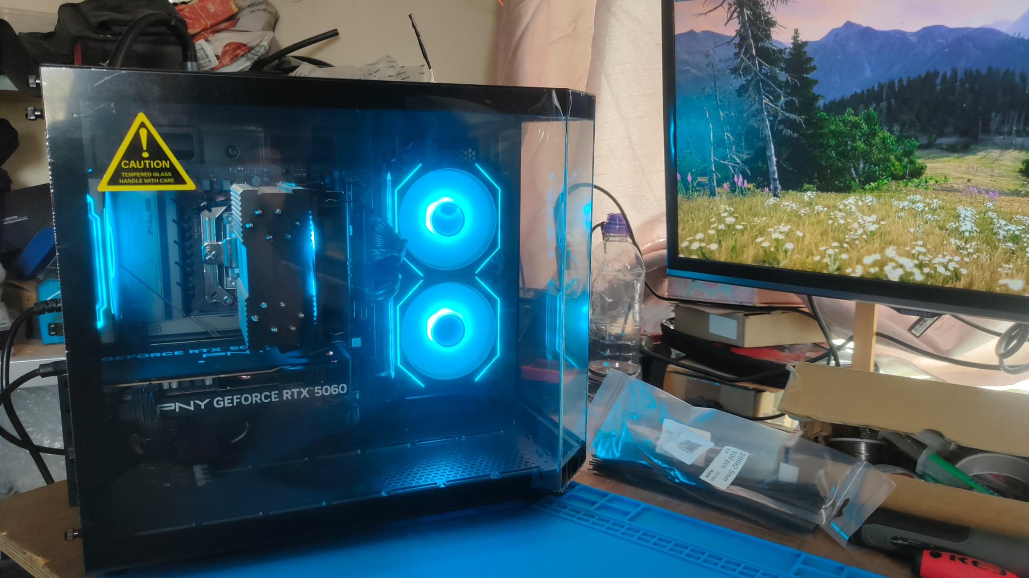 Unedited April 2026 photograph of Kirsti's finished black PC with blue lighting and PNY RTX 5060 graphics