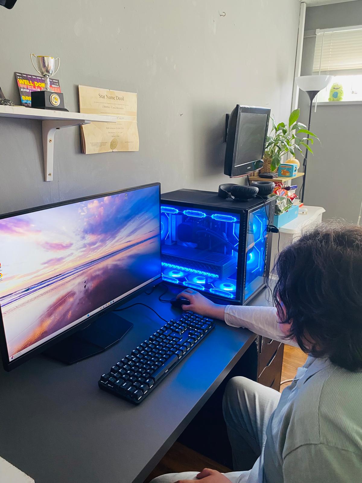 Patricia's original photo of Lorenzo at his desk with the completed blue-lit gaming PC and WQHD monitor